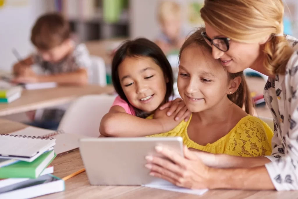 alunas e professora olhando para uma tela de um tablet