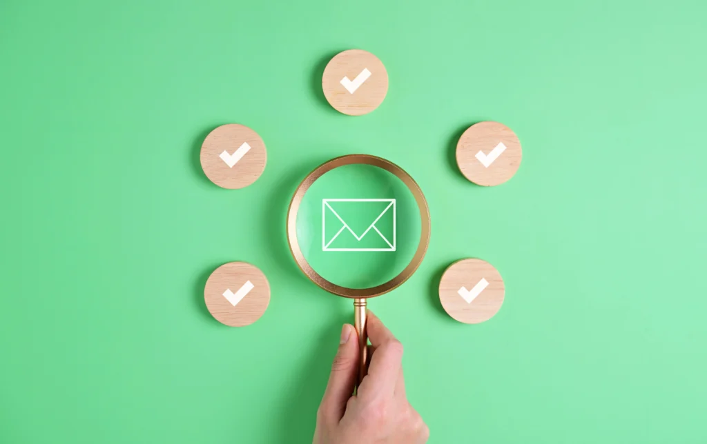 Uma mão branca, segurando uma lupa pesquisando por um símbolo de e-mail.